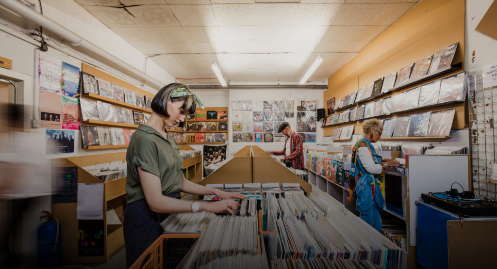 Três pessoas escolhem discos de vinil numa loja, cada uma concentrada na sua própria procura.