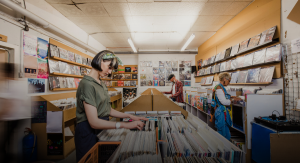Três pessoas escolhem discos de vinil numa loja, cada uma concentrada na sua própria procura.