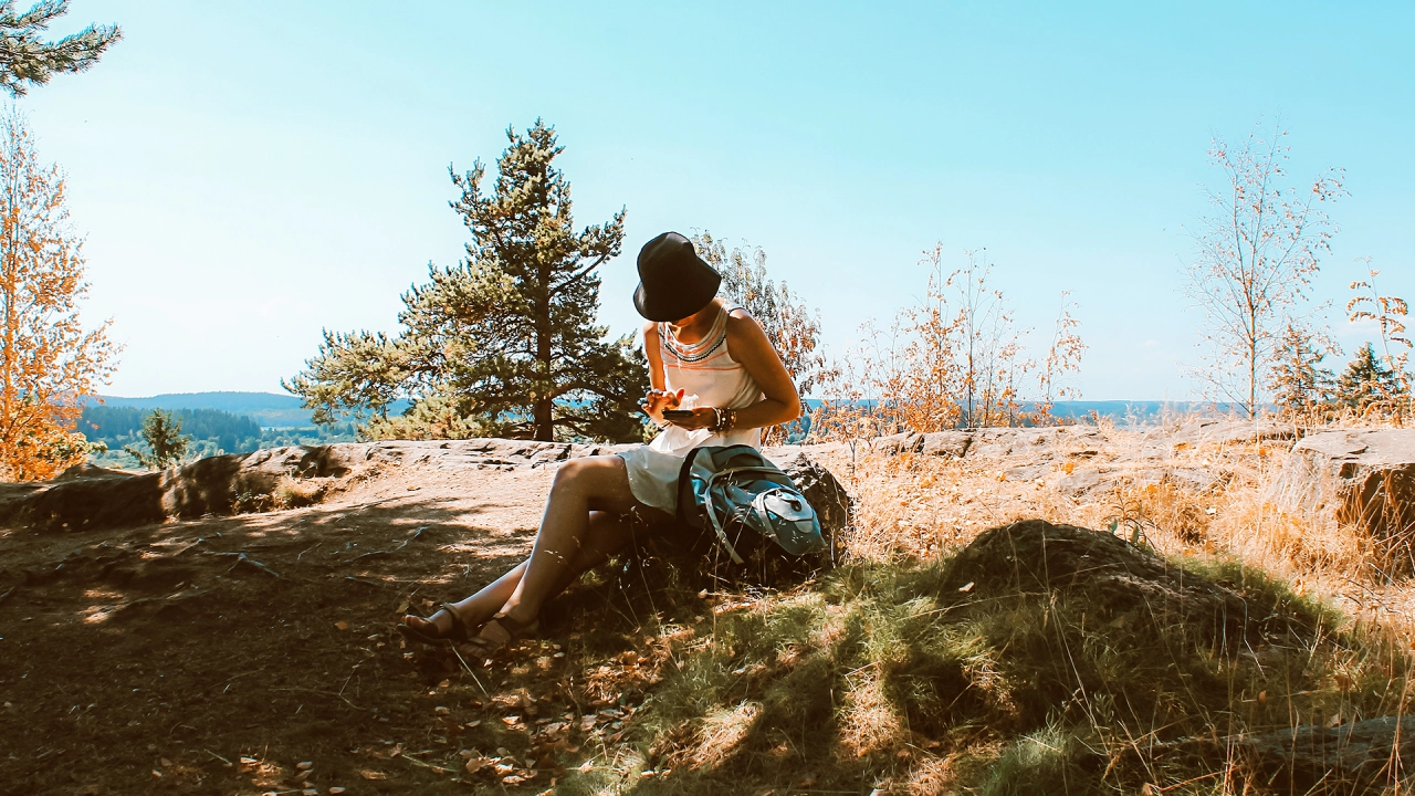 Mulher sentada num campo ao ar livre, a olhar para o horizonte, simbolizando a liberdade de estar presente e desligar do mundo digital.
