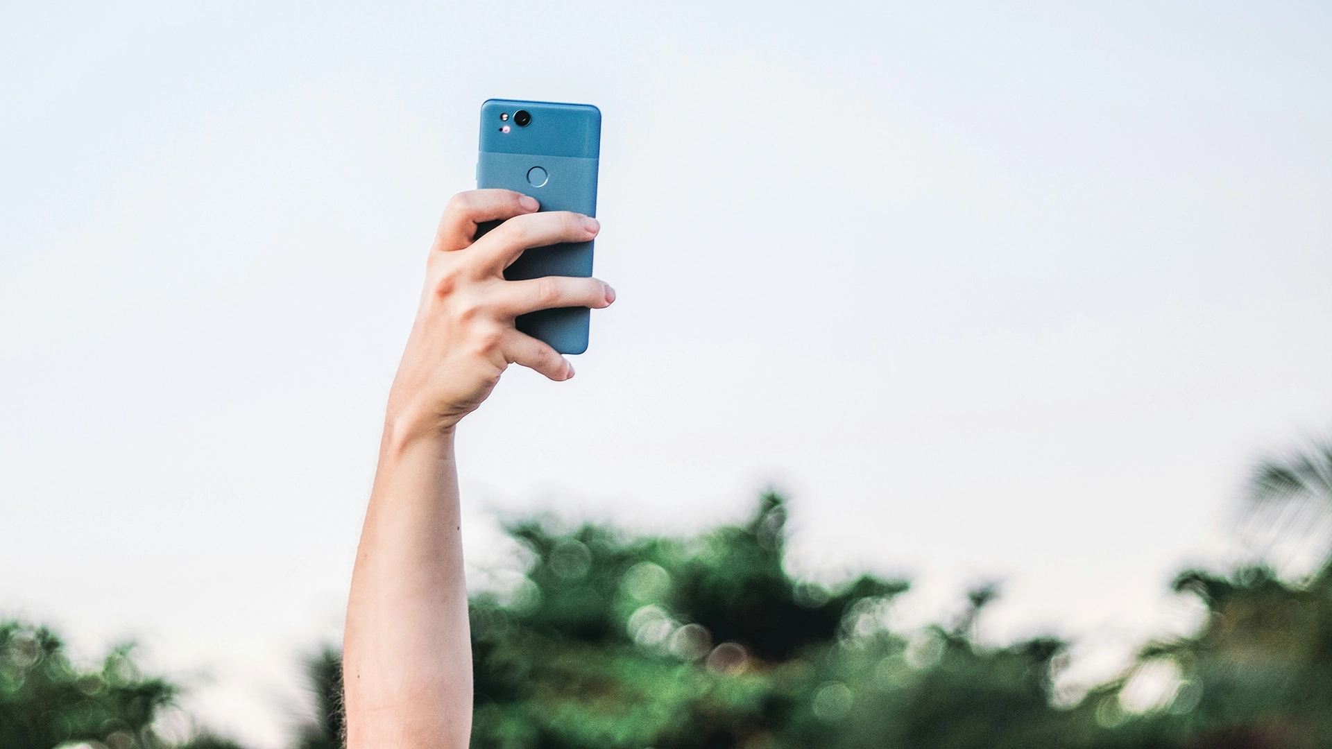 Braço estendido segurando um smartphone com o céu ao fundo, simbolizando a conectividade, alcance digital e estratégias digitais para marcas em 2024